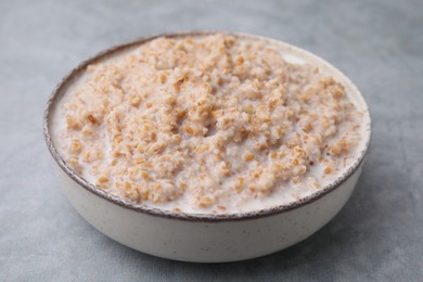 Photo of Tasty wheat porridge with milk in bowl on gray table, closeup