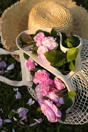 Straw hat and mesh bag with beautiful tea roses on green grass outdoors