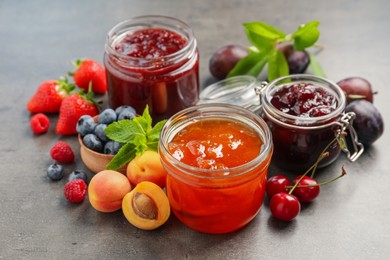 Photo of Jars with different jams and fresh fruits on grey table