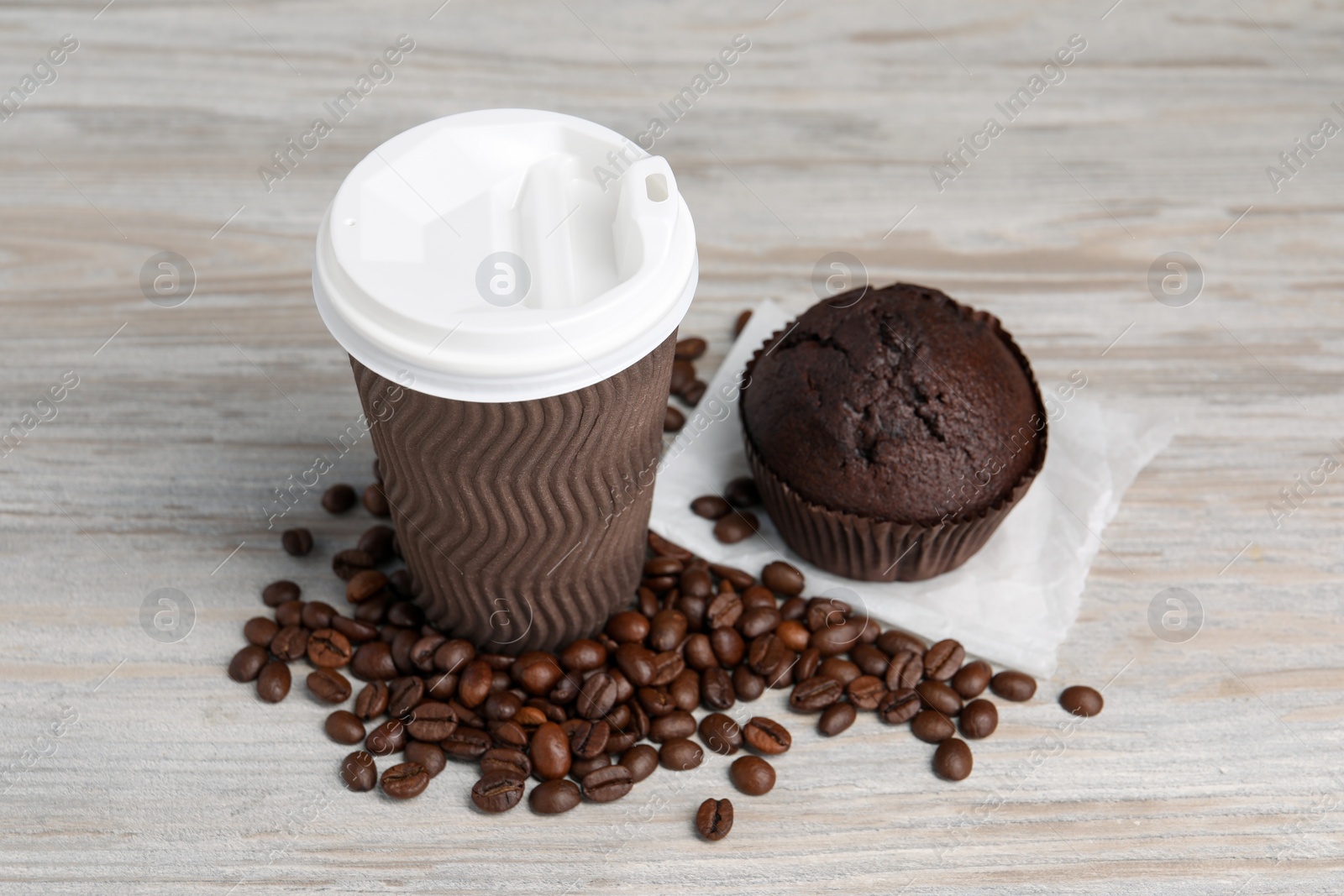 Photo of Paper cup with white lid, coffee beans and muffin on wooden table. Coffee to go