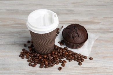 Paper cup with white lid, coffee beans and muffin on wooden table. Coffee to go