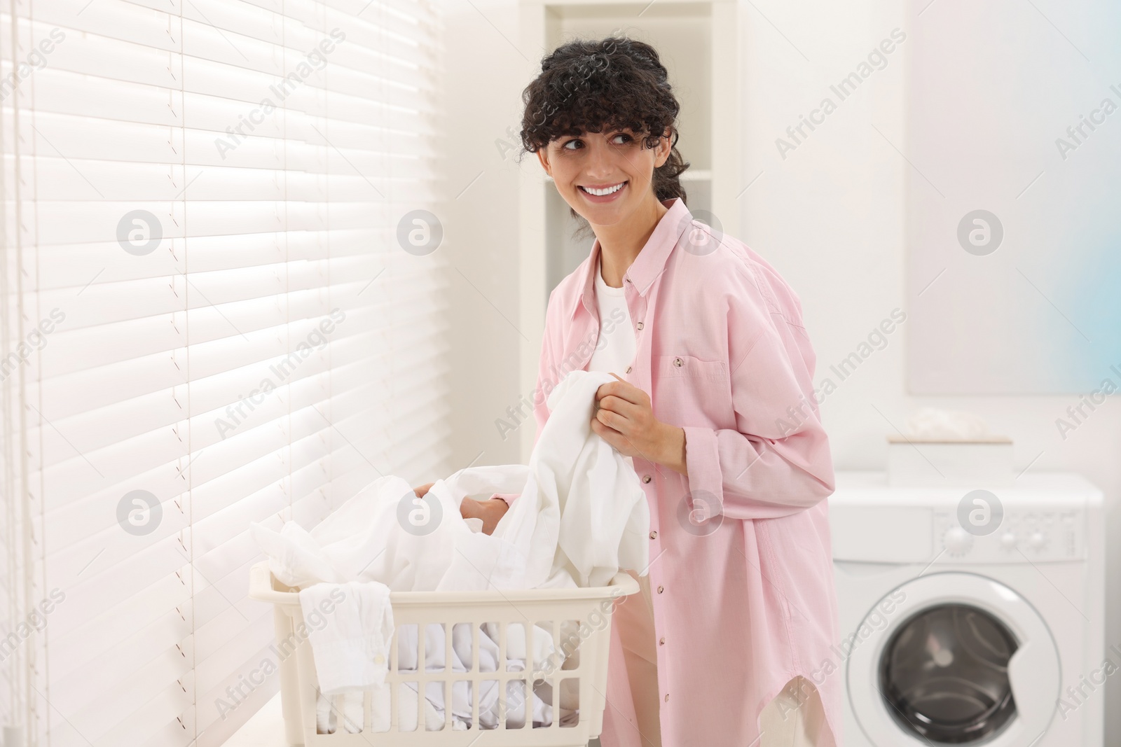 Photo of Happy woman with laundry near window indoors