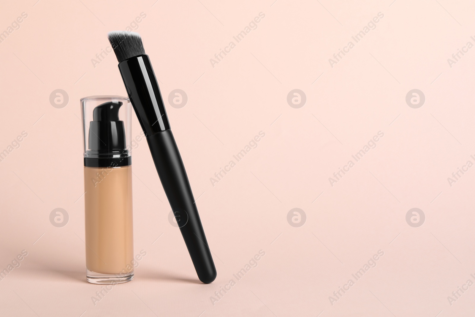 Photo of Bottle of skin foundation and brush on beige background, space for text. Makeup product