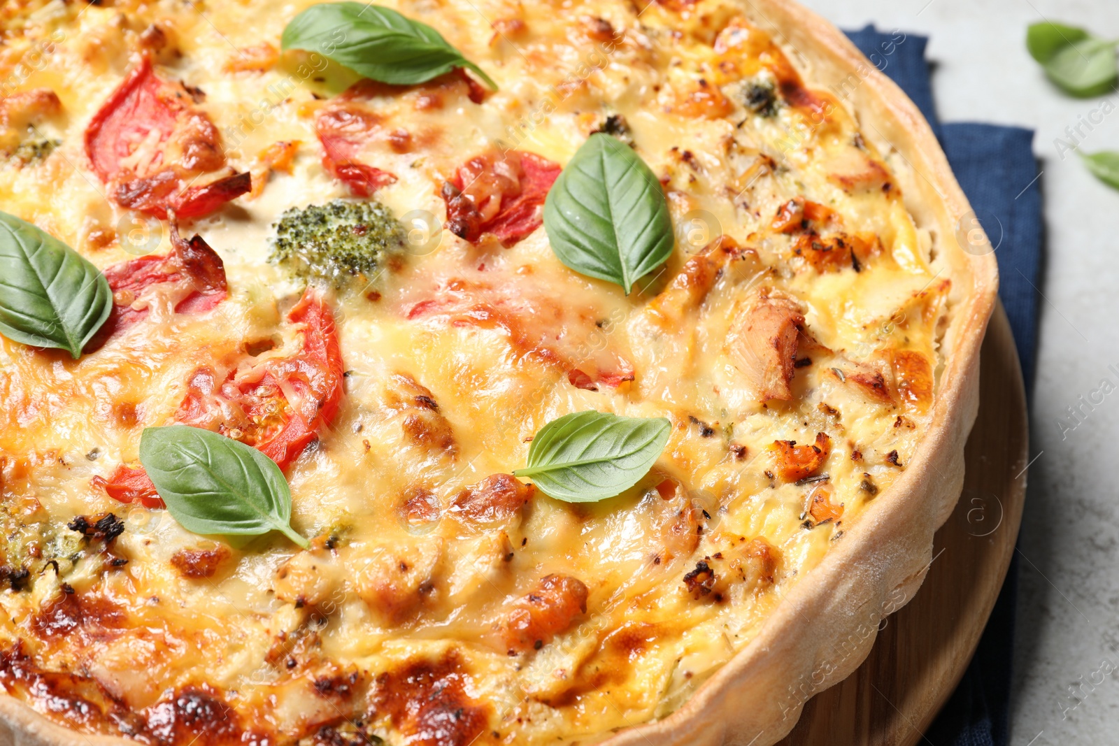 Photo of Tasty quiche with cheese, tomatoes and basil leaves on light grey table, closeup