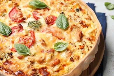 Tasty quiche with cheese, tomatoes and basil leaves on light grey table, closeup