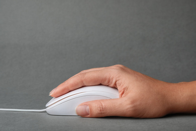 Photo of Woman using wired computer mouse on grey background, closeup