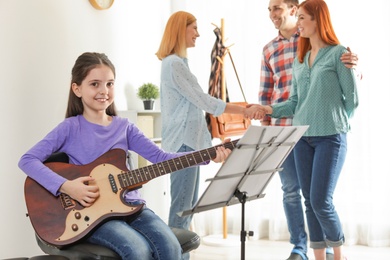 Photo of Little girl with her teacher and parents at music lesson. Learning notes