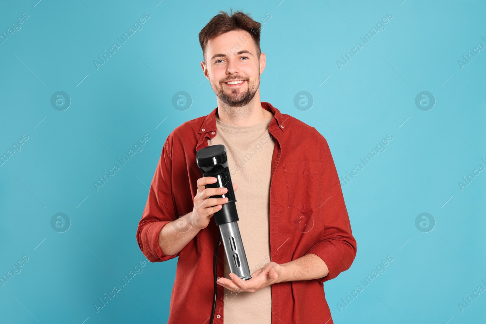 Photo of Smiling man holding sous vide cooker on light blue background