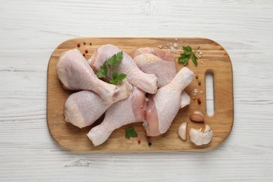 Raw chicken drumsticks with parsley, spices and garlic on white wooden table, top view