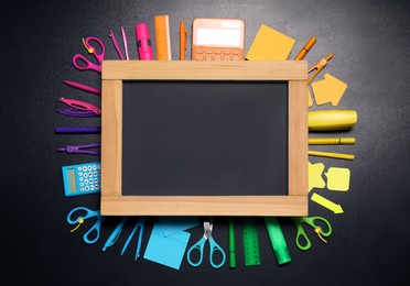 Flat lay composition with school stationery and blank chalkboard on black background, space for text