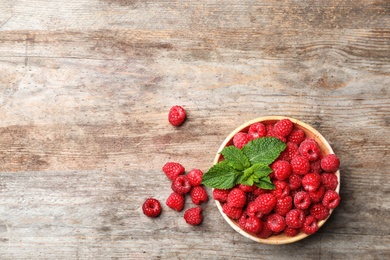 Photo of Bowl with ripe aromatic raspberries on wooden table, top view