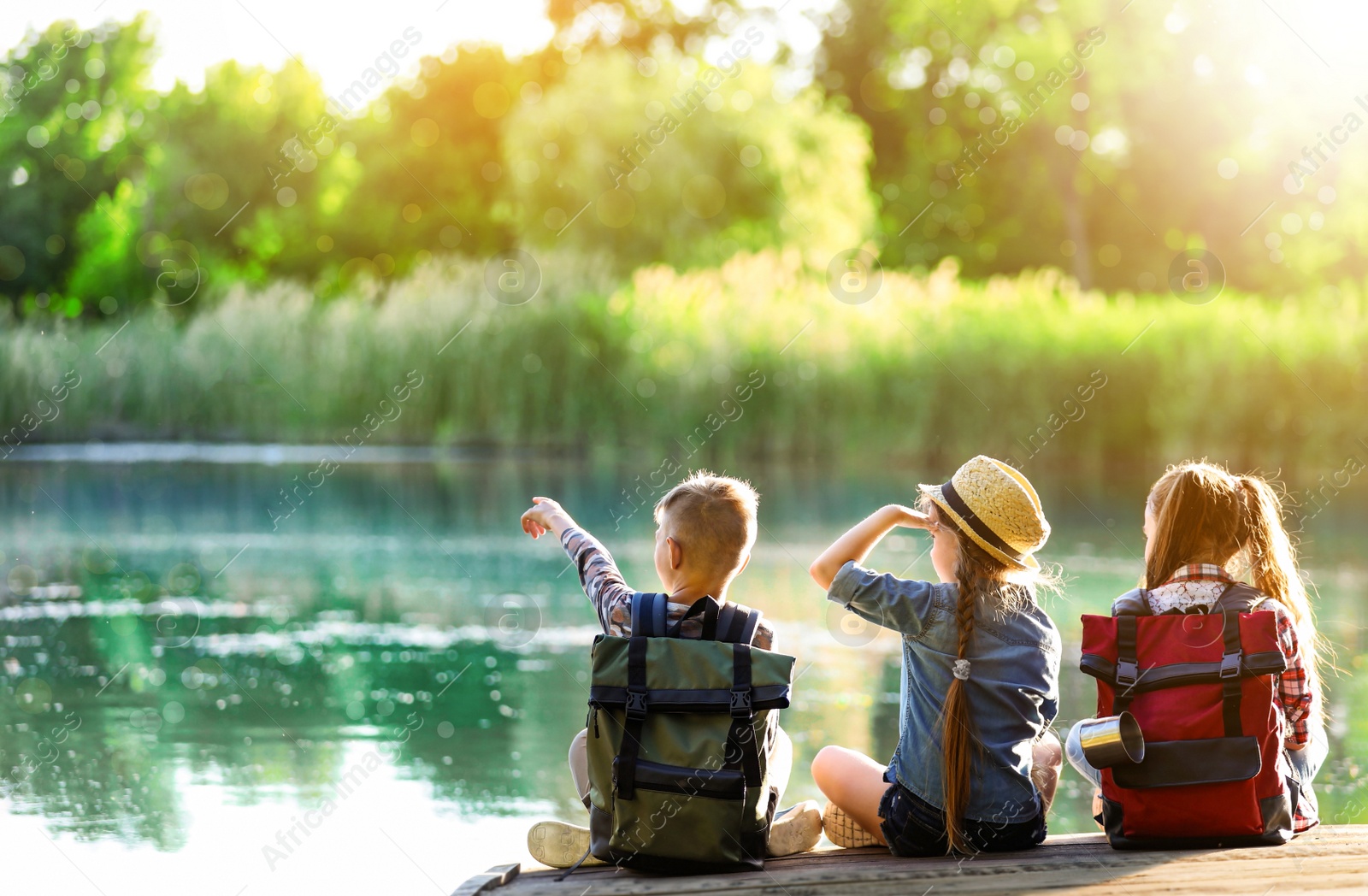 Image of School holidays. Group of children sitting on wooden pier near river 