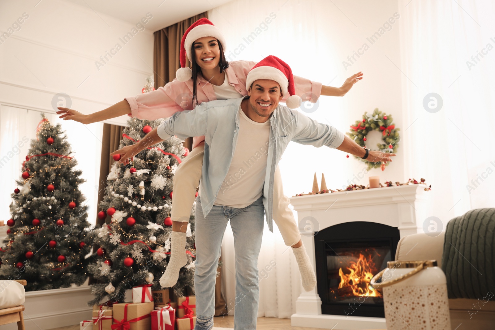 Photo of Happy couple in Santa hats near Christmas tree at home