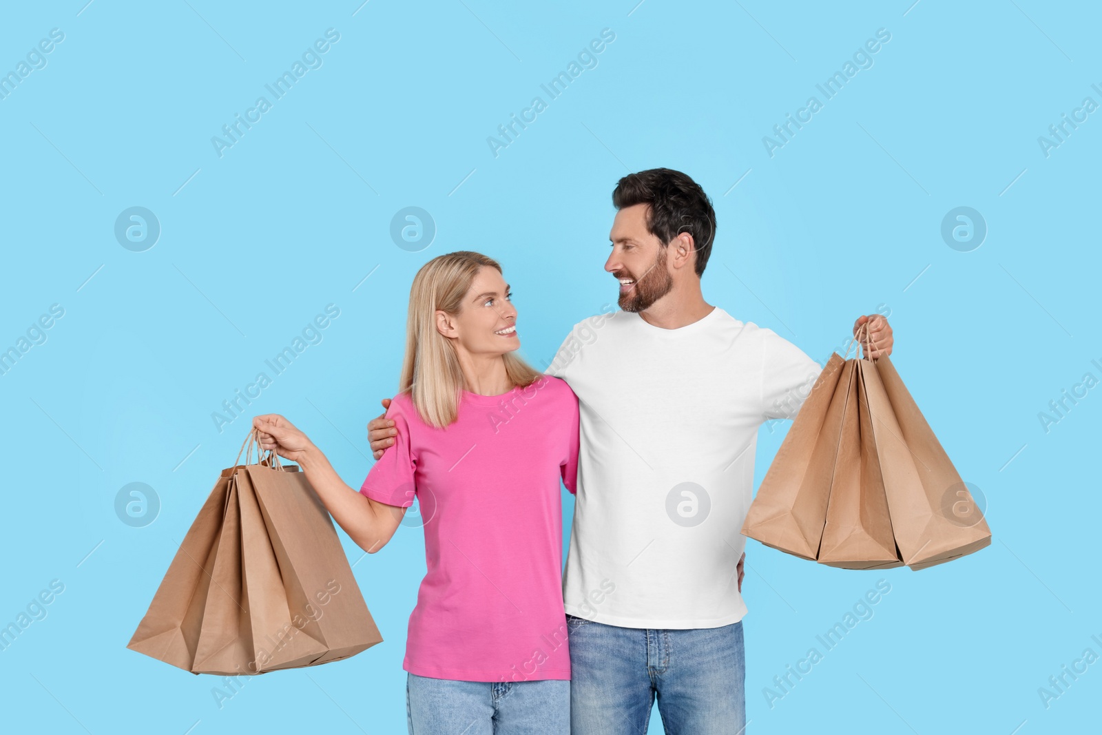 Photo of Family shopping. Happy couple with many paper bags on light blue background