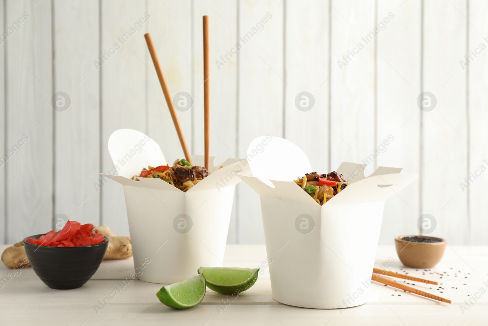 Photo of Boxes of wok noodles with vegetables, meat and chopsticks on white wooden table