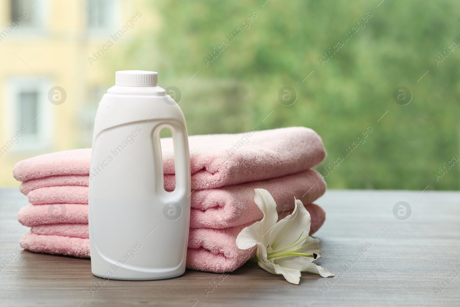 Photo of Stack of clean towels with lily and detergent on table against blurred background. Space for text