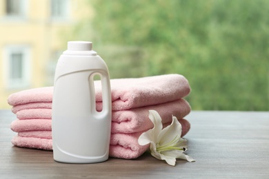 Stack of clean towels with lily and detergent on table against blurred background. Space for text