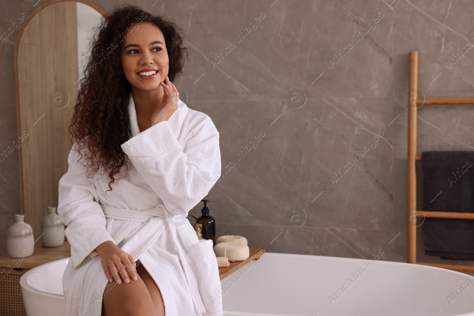 Photo of Beautiful African American woman sitting on edge of tub in bathroom, space for text