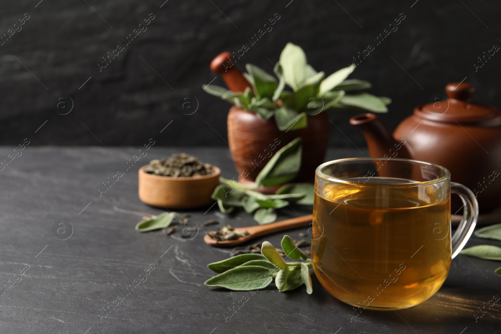 Photo of Cup of aromatic sage tea and fresh leaves on black table. Space for text