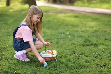 Photo of Easter celebration. Cute little girl with bunny ears hunting eggs outdoors, space for text