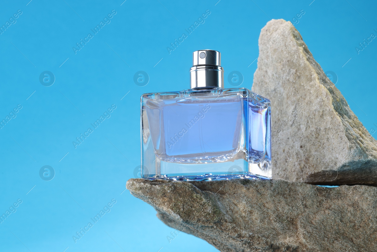 Photo of Stylish presentation of luxury men`s perfume on stones against light blue background. Space for text