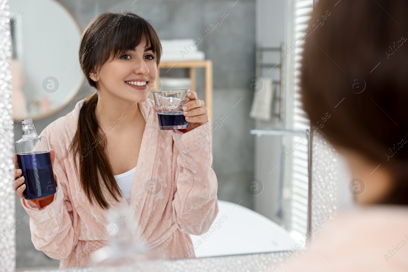 Photo of Young woman using mouthwash near mirror in bathroom