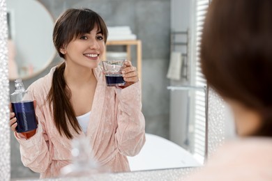 Young woman using mouthwash near mirror in bathroom