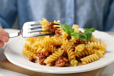 Photo of Woman eating delicious pasta with minced meat and basil at table, closeup