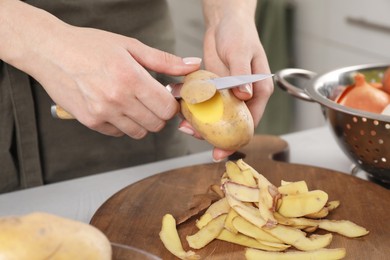 Woman peeling fresh potato with knife at table indoors, closeup