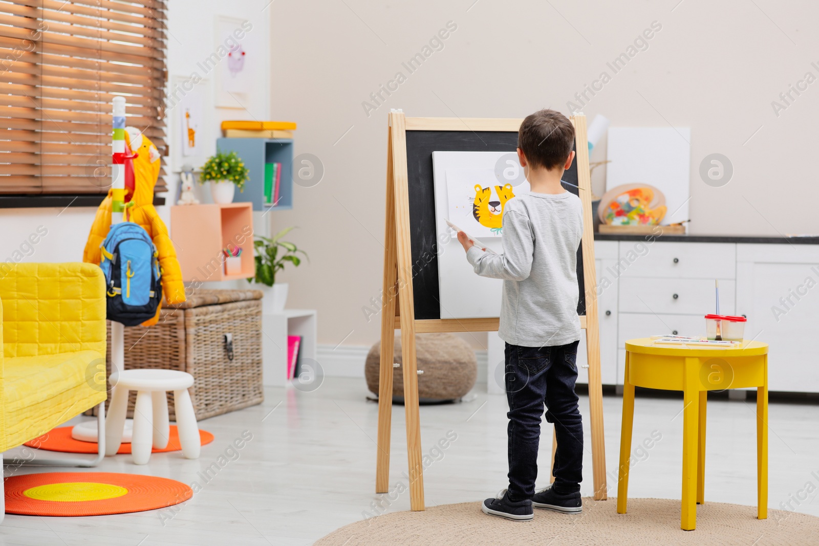 Photo of Little child painting on easel in room