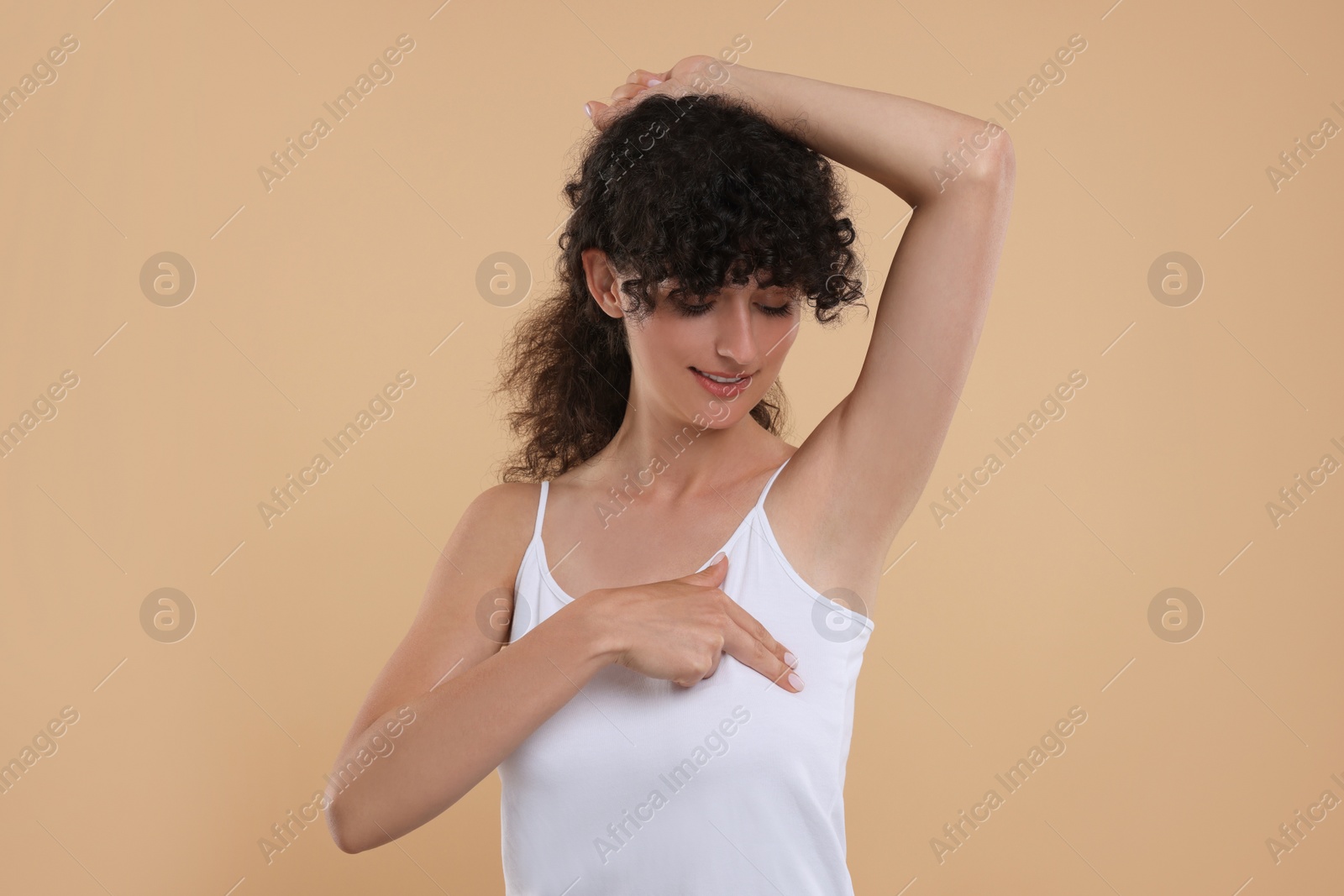 Photo of Beautiful young woman doing breast self-examination on light brown background