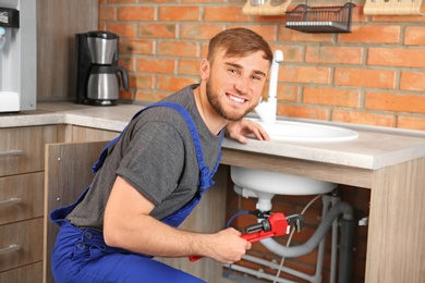 Professional plumber in uniform with pipe wrench near kitchen sink