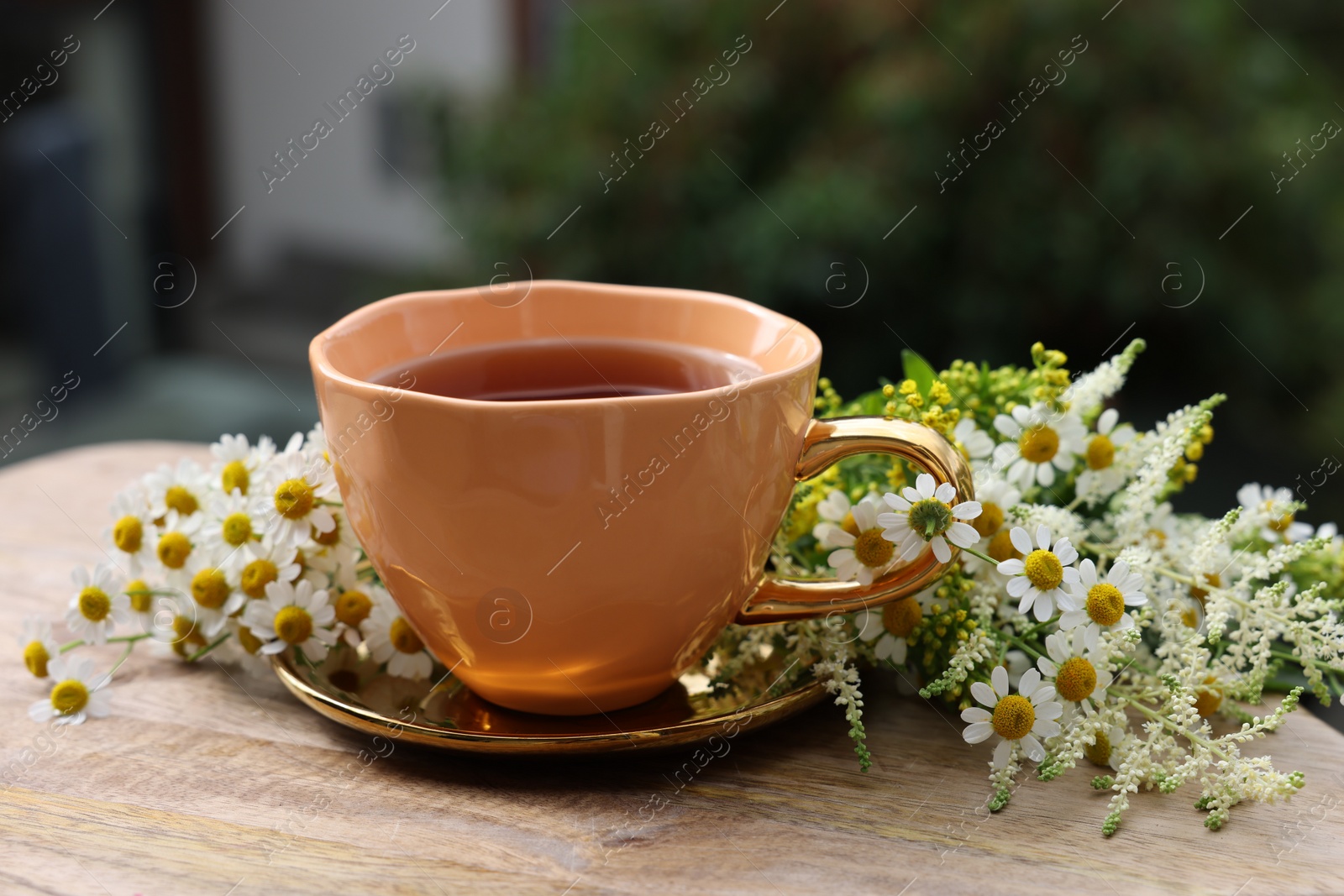 Photo of Cup of delicious chamomile tea and fresh flowers outdoors