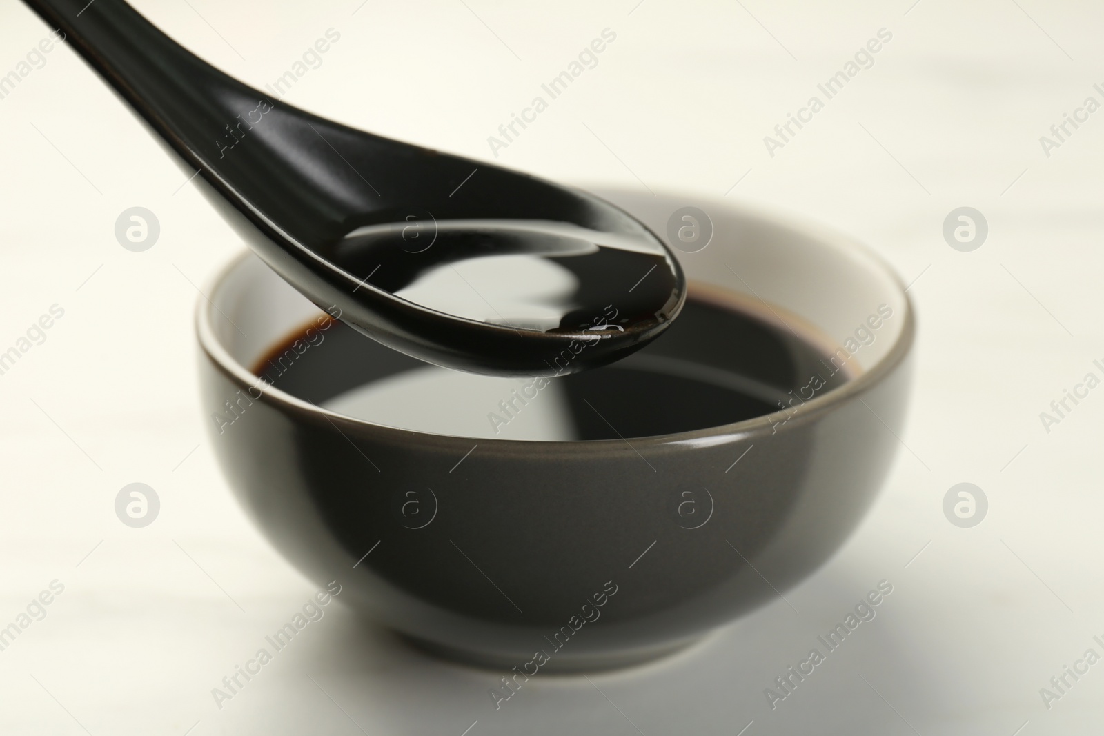 Photo of Taking soy sauce with spoon from bowl at white table, closeup