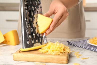 Woman grating fresh cheese at table, closeup