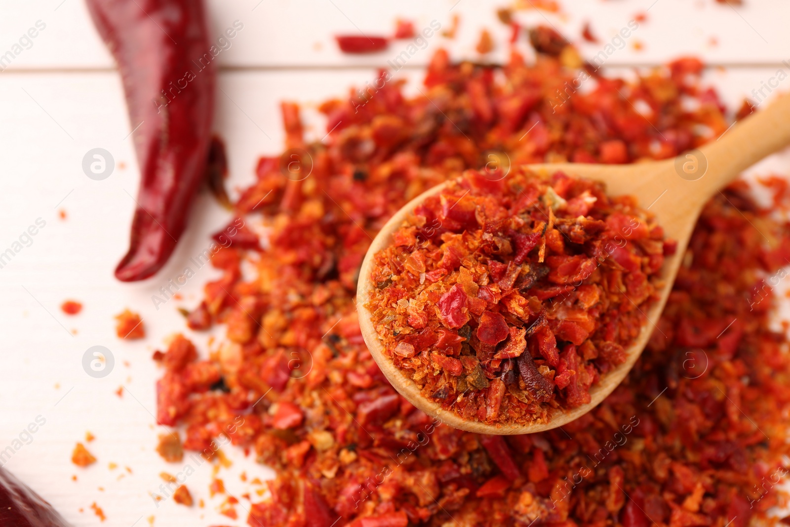 Photo of Chili pepper flakes and pod on white wooden table, closeup