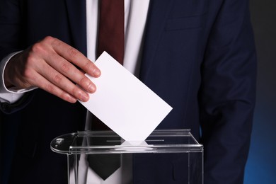 Photo of Man putting his vote into ballot box on dark background, closeup