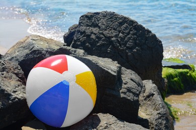Photo of Colorful beach ball among rocks at seaside on sunny day