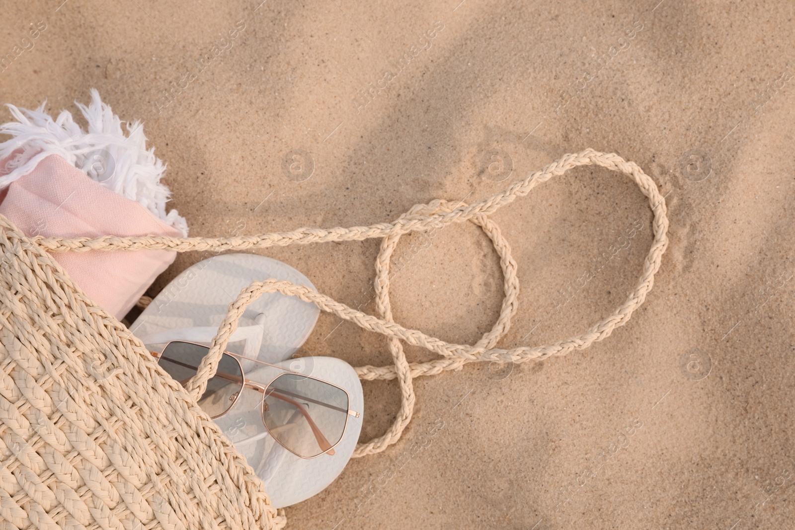 Photo of Beach bag with flip flops, towel and sunglasses on sand, top view. Space for text