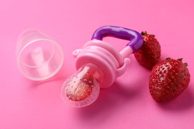 Photo of Nibbler with fresh strawberries on pink background. Baby feeder