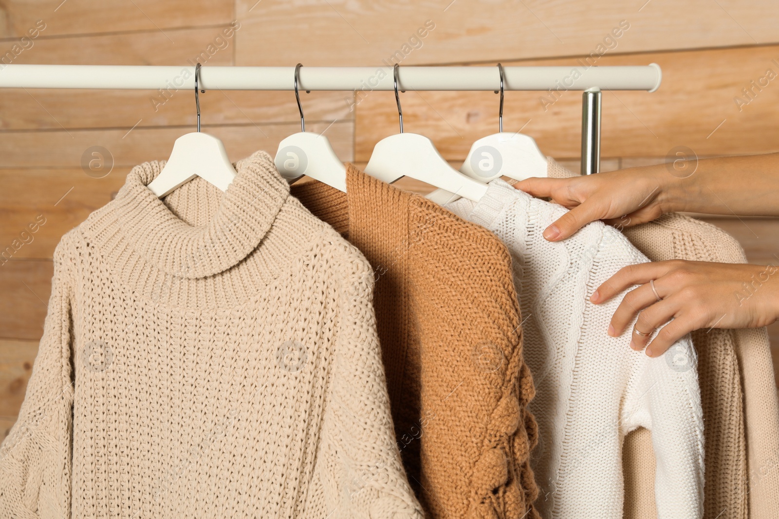 Photo of Woman choosing sweater on rack against wooden background