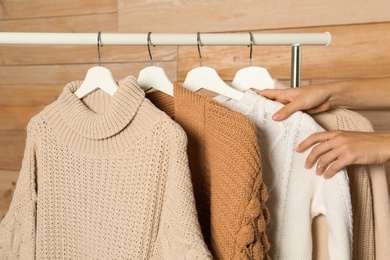 Woman choosing sweater on rack against wooden background