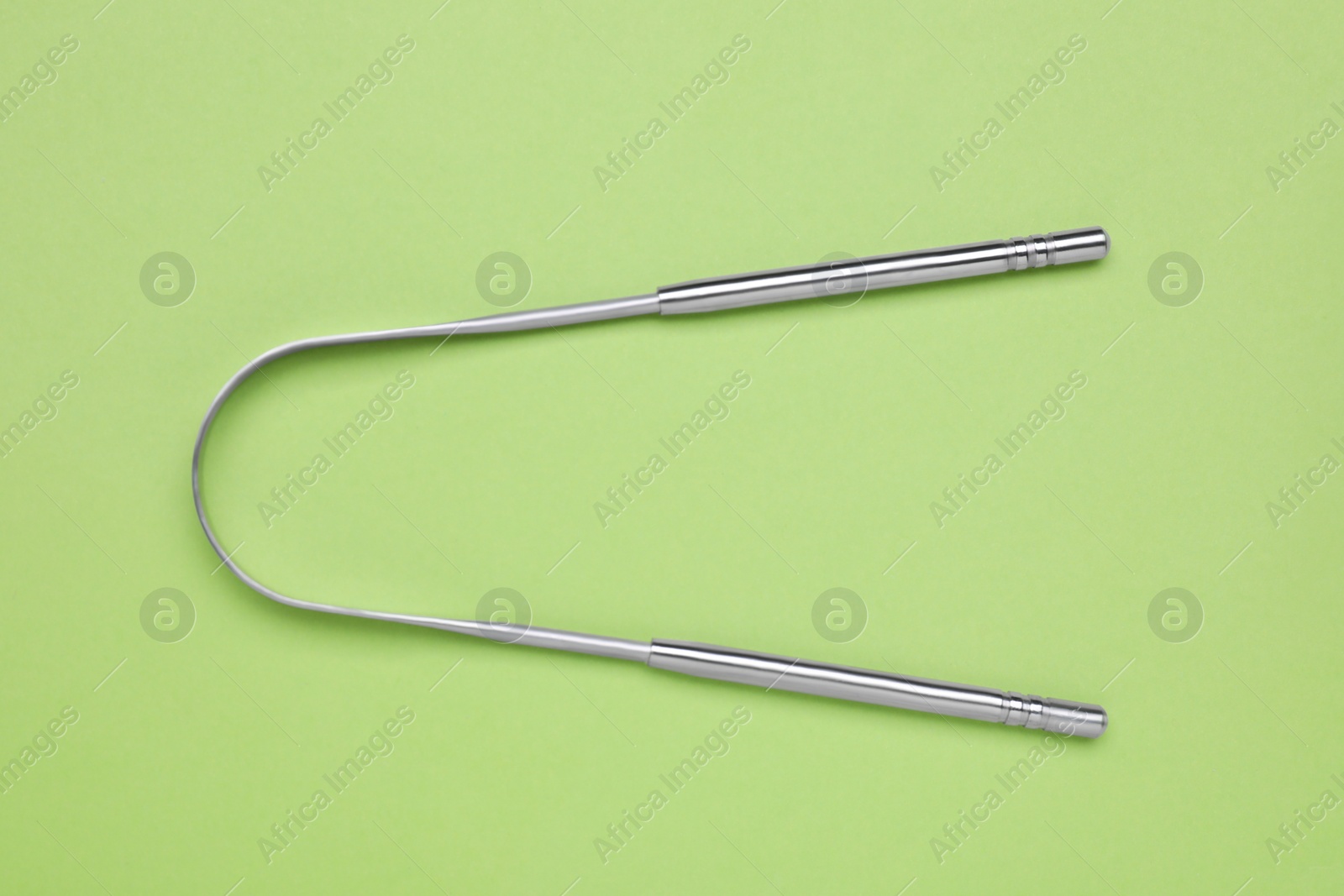 Photo of Metal tongue cleaner on light green background, top view