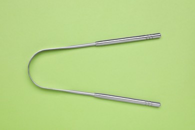 Photo of Metal tongue cleaner on light green background, top view