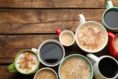 Many cups of different coffees on wooden table, flat lay. Space for text