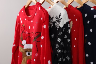 Photo of Different Christmas sweaters hanging on rack against light background, closeup
