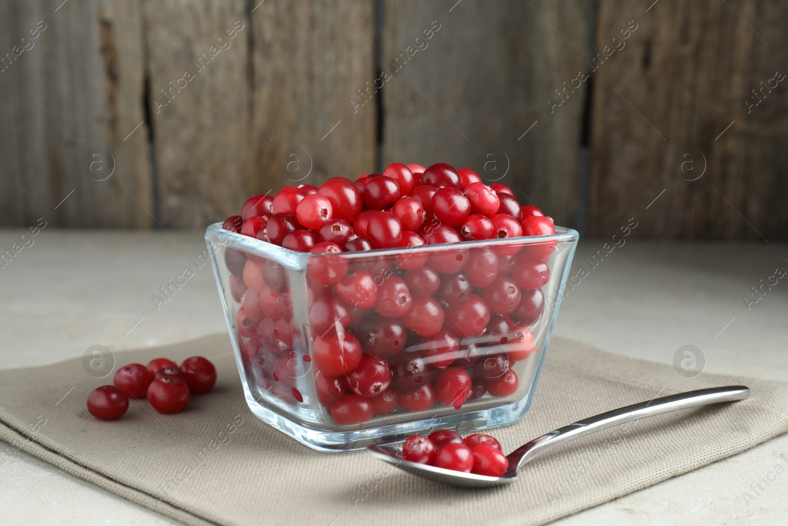 Photo of Cranberries in bowl and spoon on light grey table, closeup