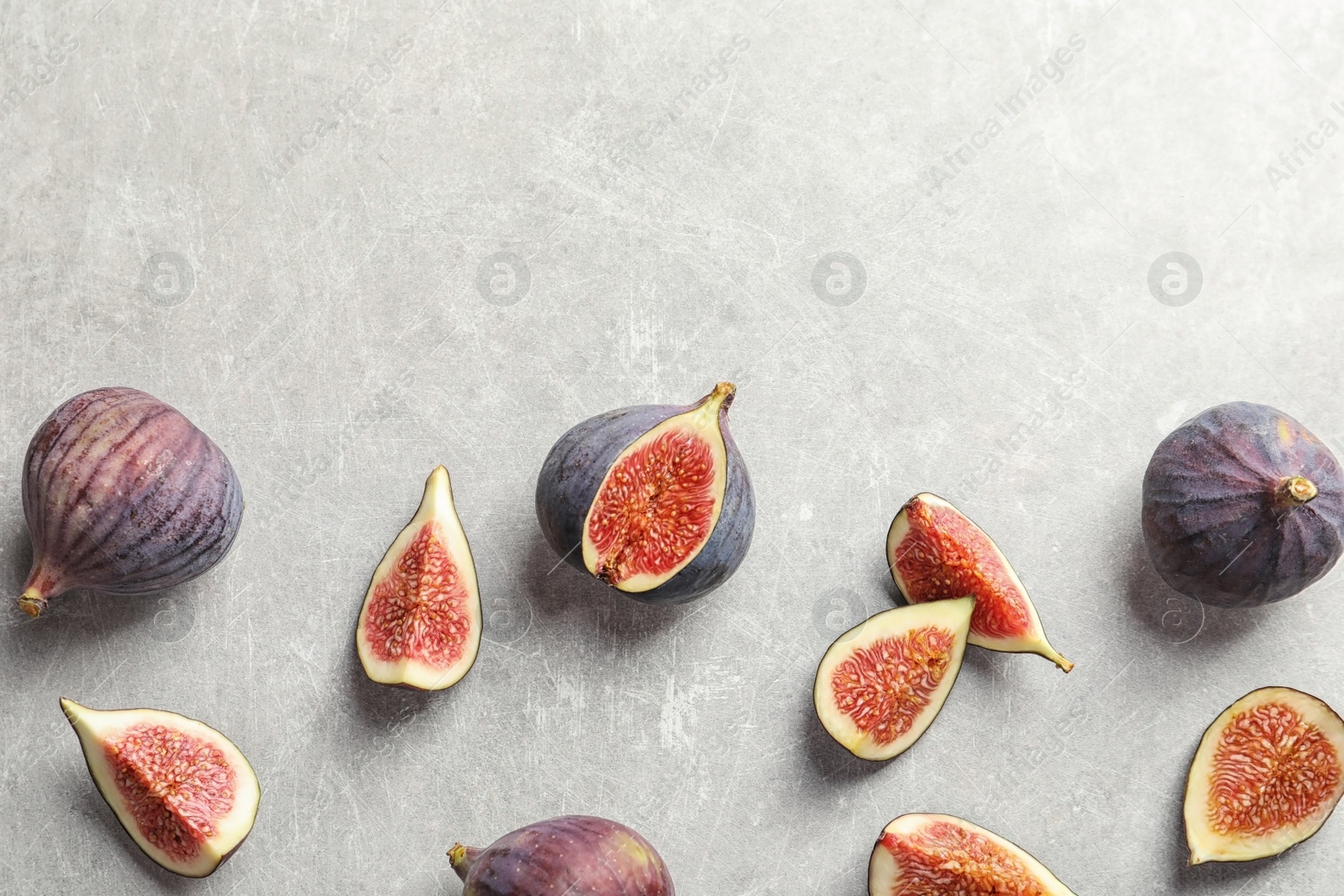 Photo of Flat lay composition with whole and cut purple figs and space for text on gray background