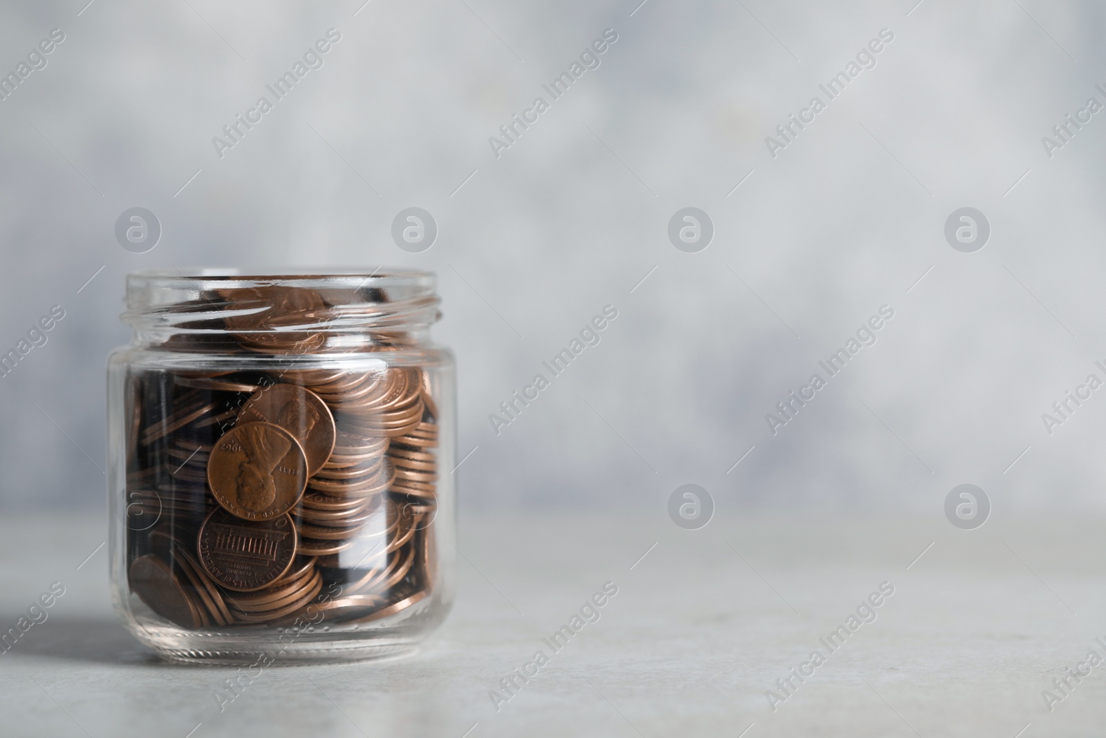 Photo of Glass jar with coins on light grey table, closeup. Space for text