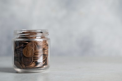 Glass jar with coins on light grey table, closeup. Space for text